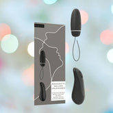 The B Swish Bnaughty Deluxe Unleashed - Black boxed set highlights a remote-controlled intimate massager, elegantly designed with silhouette artwork on its packaging. This sleek, curved, and waterproof device comes with a slender cord and is beautifully presented against a blurred, multicolored background for an enticing display.